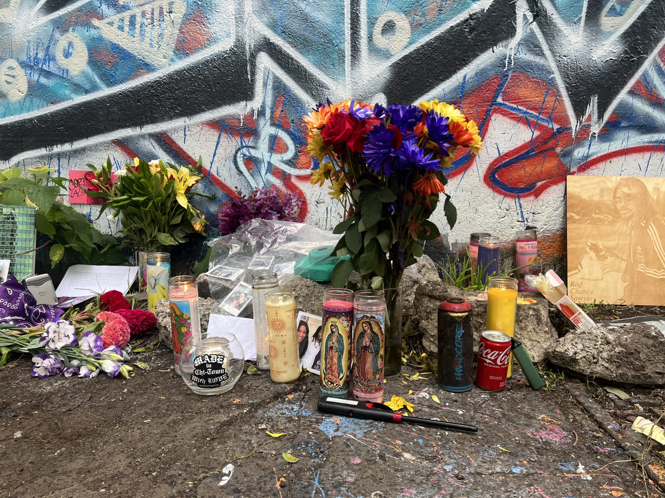 Memorial para Rod con flores, velas y objetos personales frente a su obra de grafiti.
