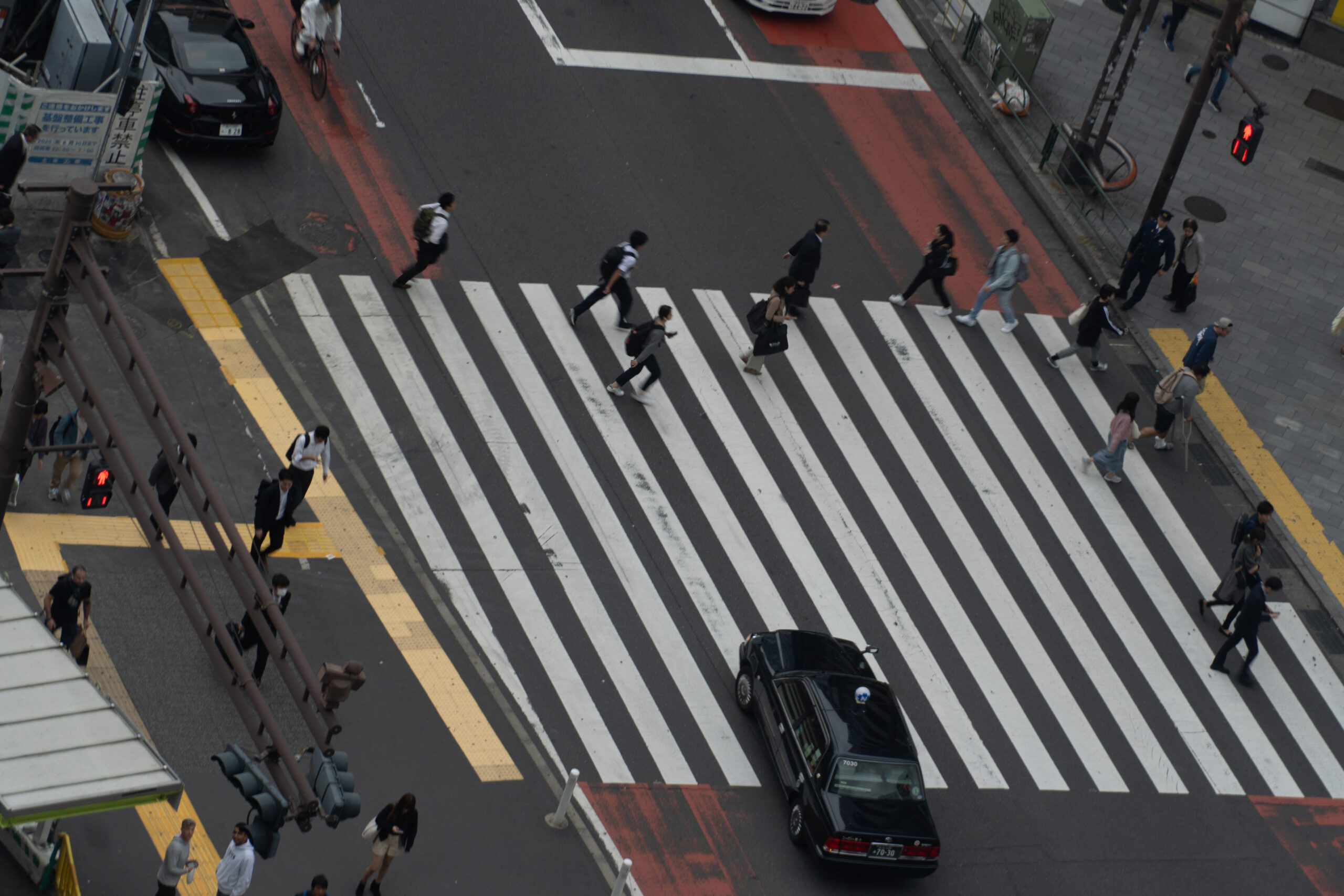 Pedestrians crossing a striped city crosswalk in Japan, viewed from above